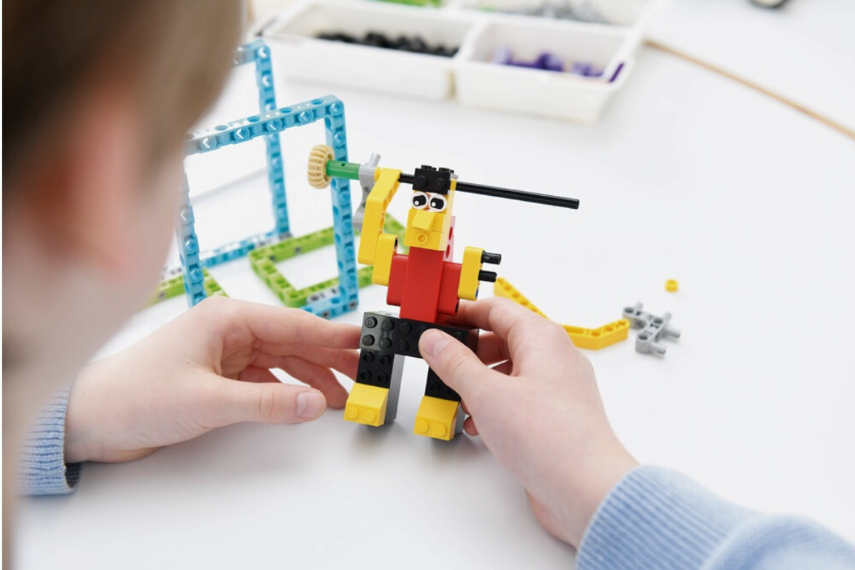model z klocków lego ludzik w czerwonej koszulce podnoszący ciężar, chłopiec składa model na białym stoliku